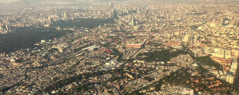 Anflug im Sonnenuntergang auf das Häusermeer von Mexiko City mit dem Bosque de Chapultepec.